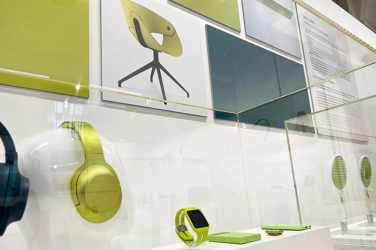 Exhibición con audífonos verdes, un reloj inteligente y el diseño de una silla sobre una pared blanca con paneles verdes