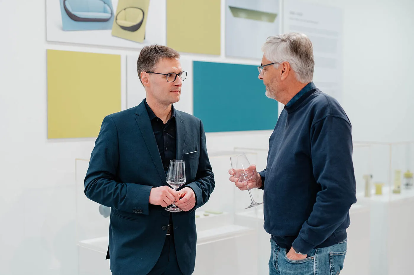 Dos hombres hablando en una exposición de diseño con paneles de pared coloridos y expositores de productos