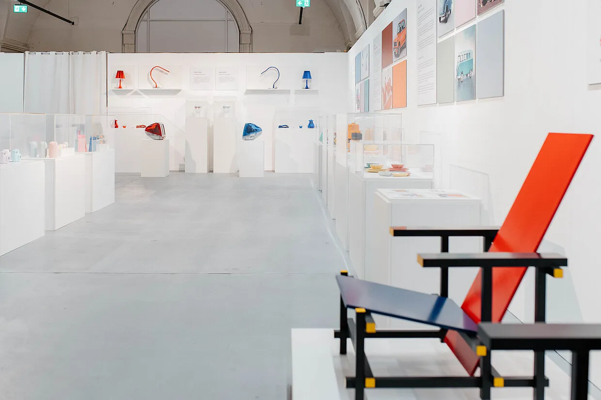 Interior de designforum Wien con una silla roja y azul en primer plano y objetos de diseño en exhibición