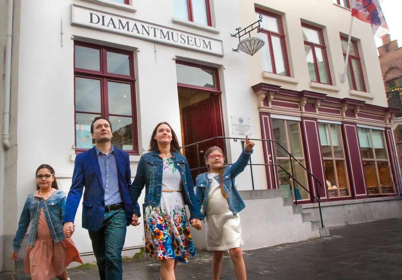 Una familia de cuatro personas de pie frente a la fachada blanca del edificio del Diamantmuseum, mirando hacia el cartel sobre la entrada.