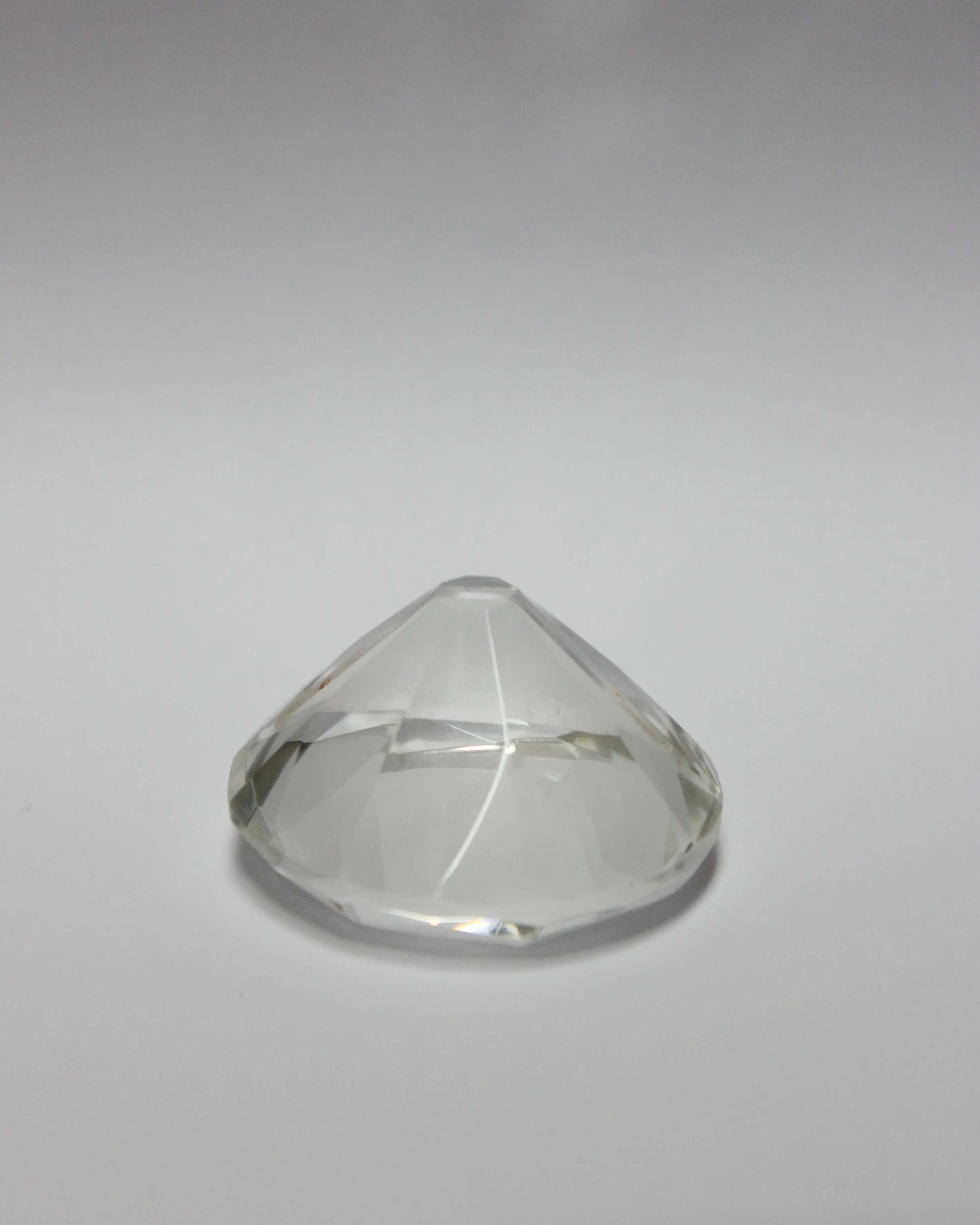Una gema transparente con forma de diamante y caras facetadas sobre un fondo gris claro sencillo.