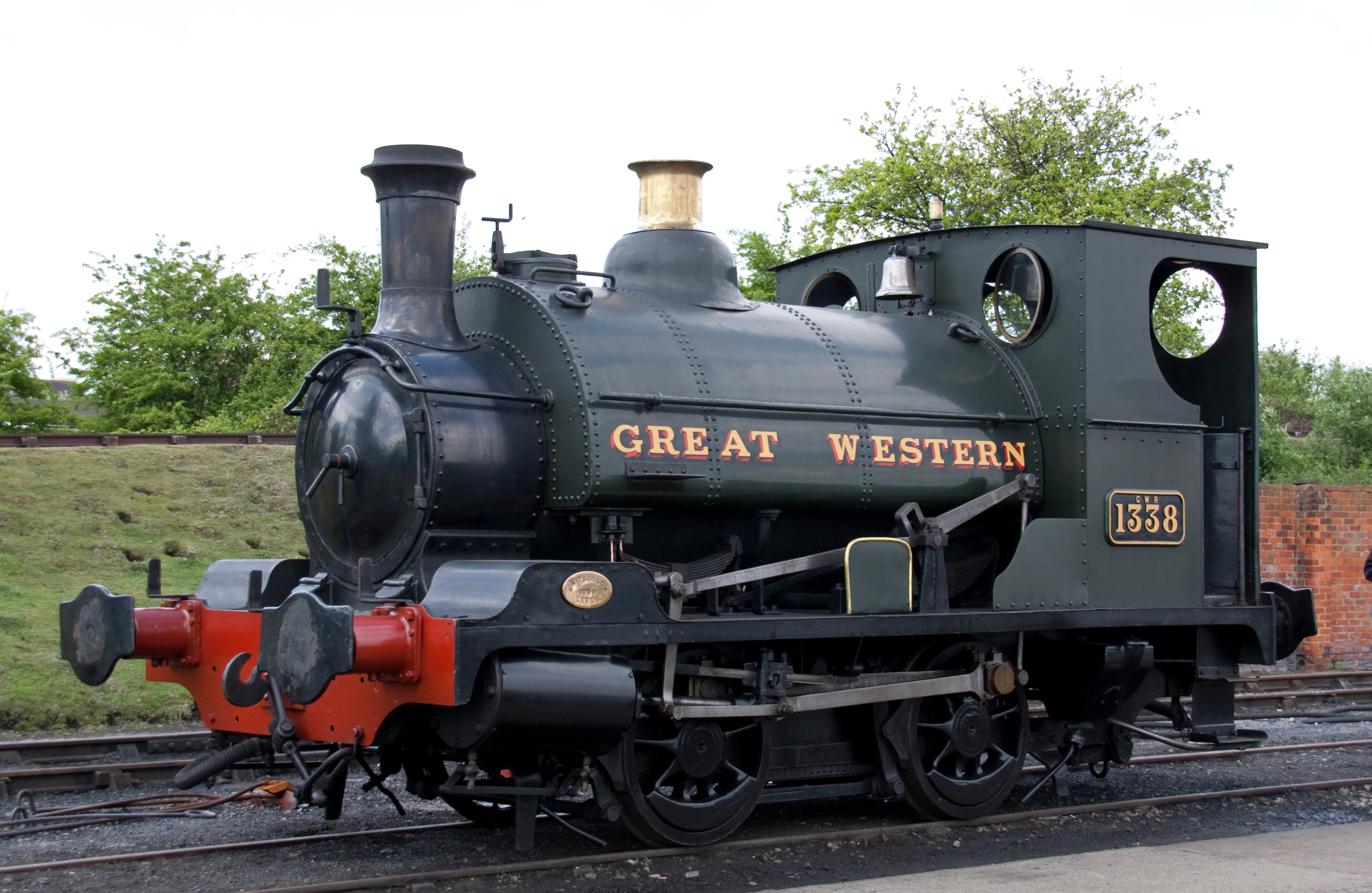 Ciemnozielona lokomotywa parowa z czerwonymi belkami zderzakowymi, oznaczona napisem 'GREAT WESTERN' i numerem 1338, stojąca na torach kolejowych.