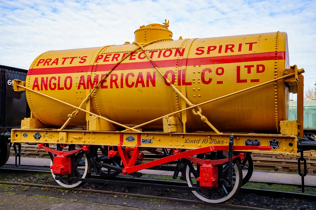Żółty cylindryczny wagon cysterna z czerwonym napisem 'Pratt's Perfection Spirit Anglo American Oil Co Ltd' na czerwonej ramie z kołami o białych obwódkach