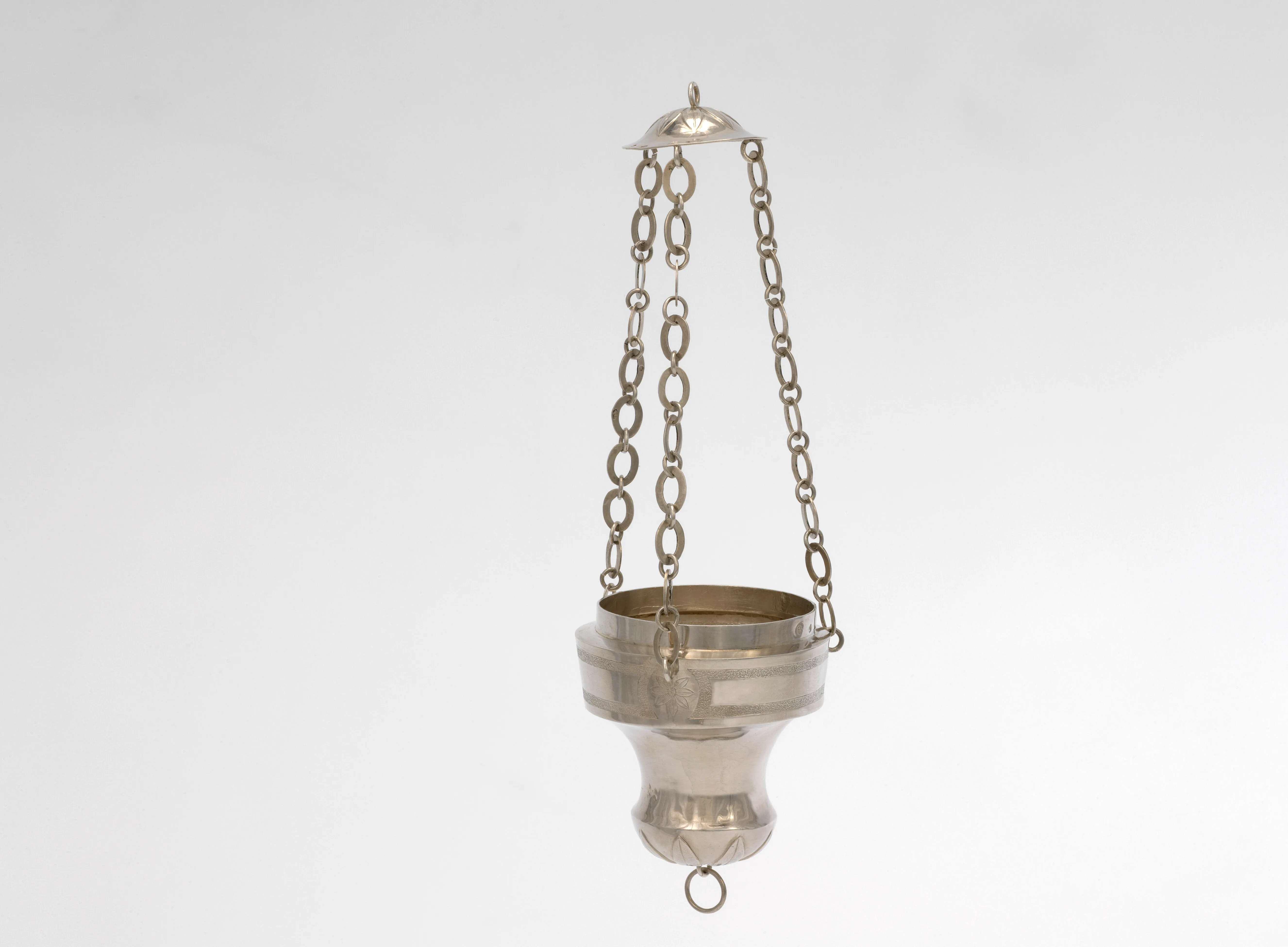 Lámpara de santuario colgante de plata suspendida por tres cadenas sobre un fondo blanco, con una parte superior abovedada y un anillo en la base.