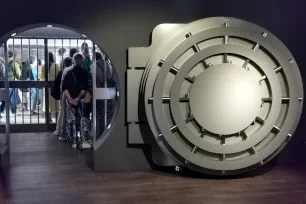 Gran puerta circular de metal de una cámara acorazada de banco, abierta en la sala de un museo con visitantes visibles a través del vano