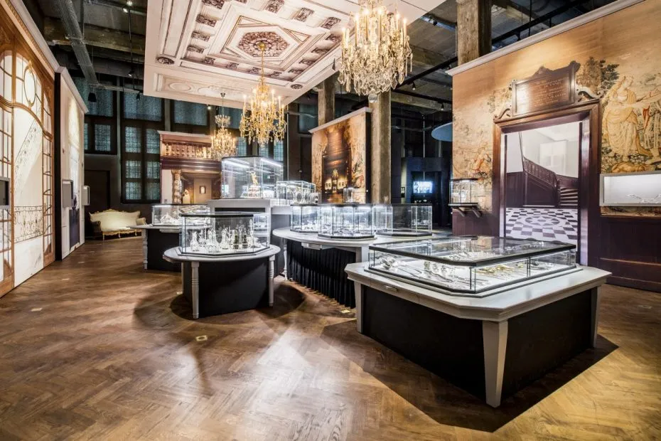Interior del museo DIVA que muestra vitrinas de cristal con joyas, lámparas de araña, un techo ornamentado y grandes murales en una gran sala de exposiciones con suelos de madera.