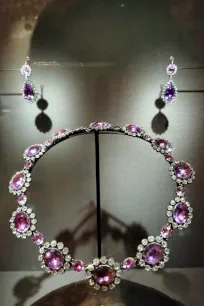 Museum display case showing a necklace and matching earrings set with large pink-purple gemstones surrounded by diamonds under spotlights