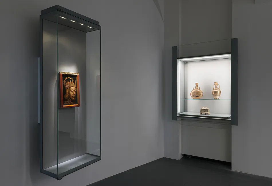 Twee glazen vitrines in een museumgalerij, één met een ingelijst kunstwerk en de andere met gouden objecten