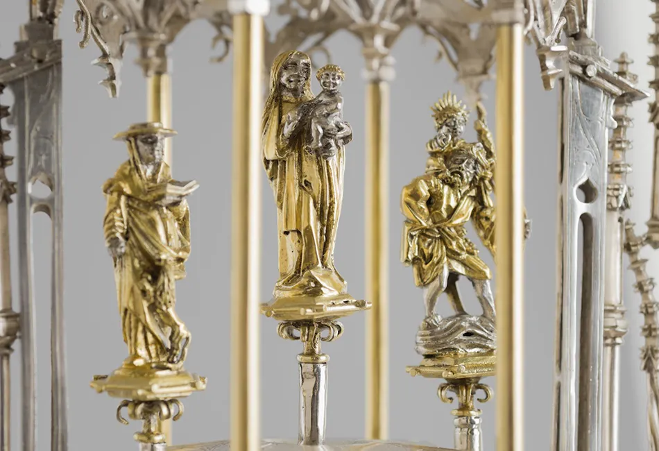 Gouden religieuze sculpturen van figuren op sokkels in een decoratieve zilveren en gouden kandelaar