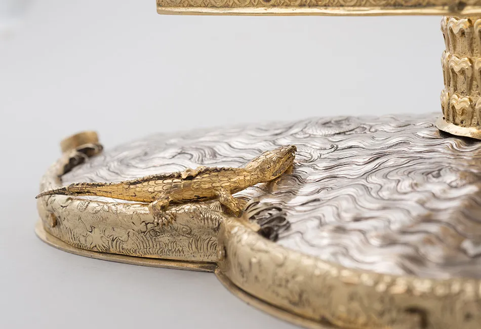 close-up van een verguld krokodillenfiguur op een zilveren en gouden religieus artefact