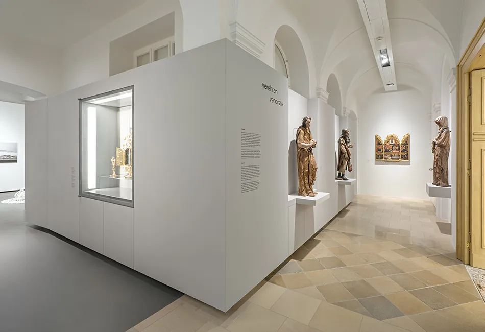 Witte galerijgang met gewelfde plafonds, met gouden beelden en een glazen vitrine