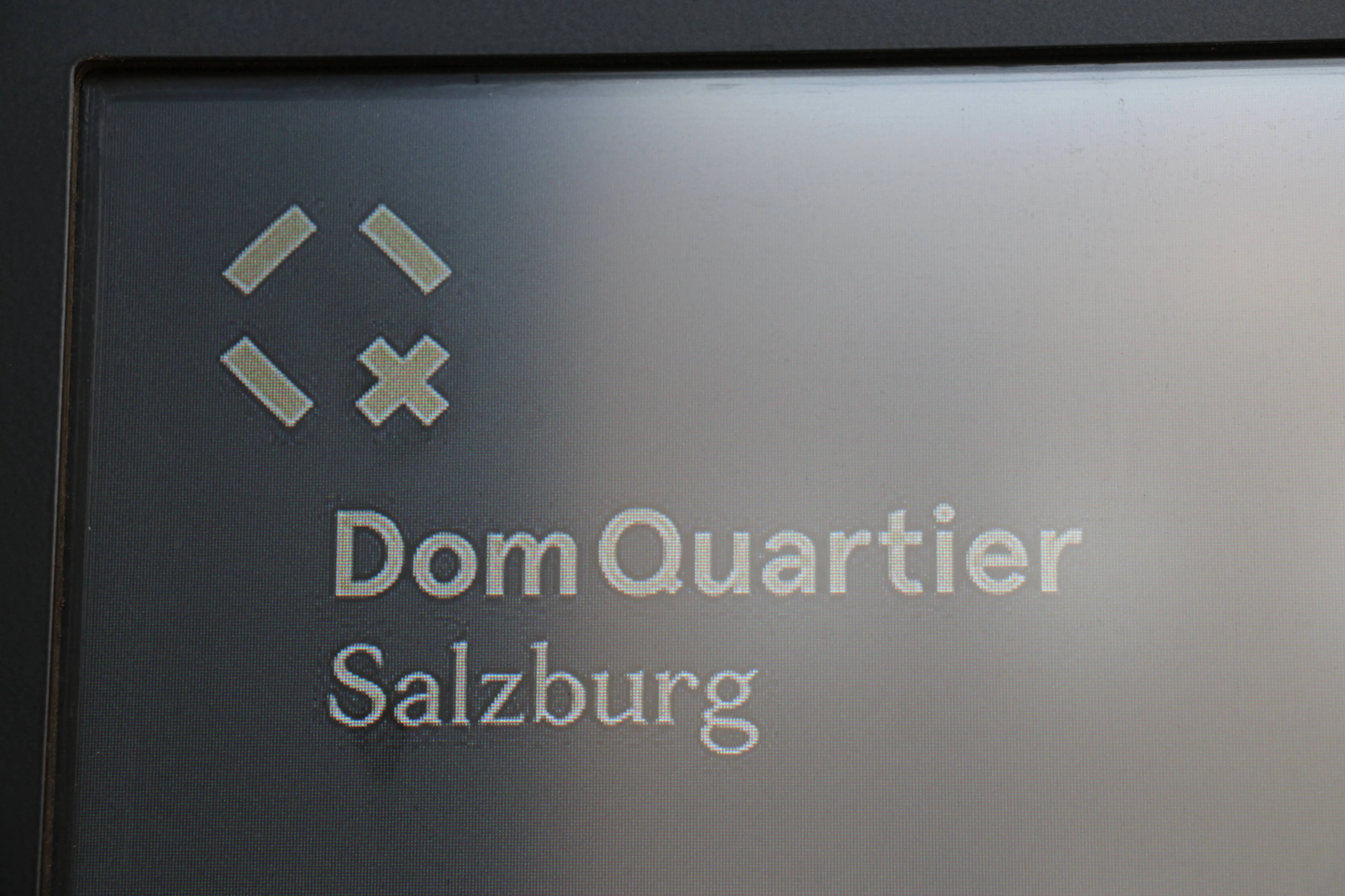 DomQuartier Salzburg wordmark with stylized four-diamond emblem on a dark metallic sign