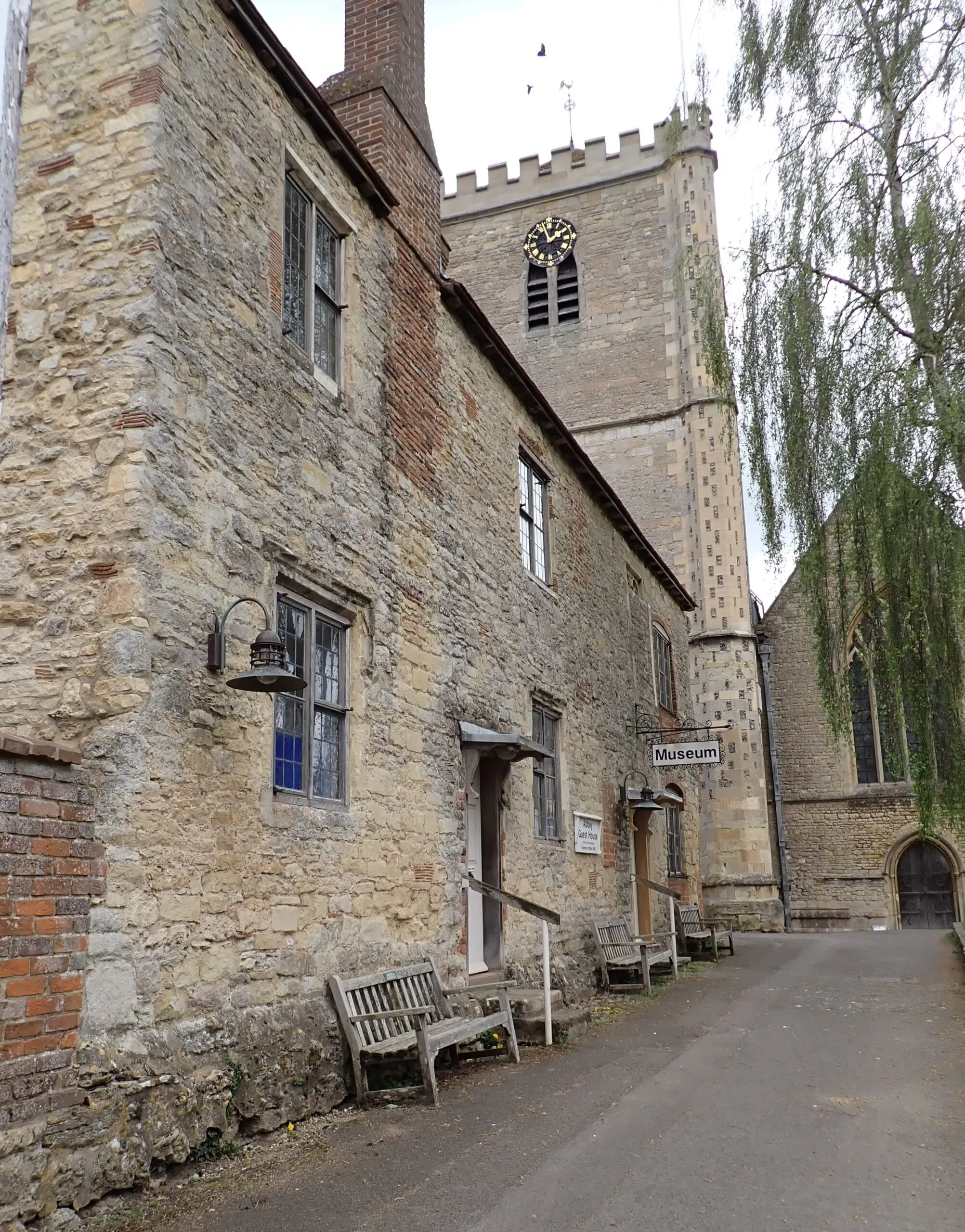 Exterior view of a stone building with a Museum sign, next to a tall church tower with a clock.