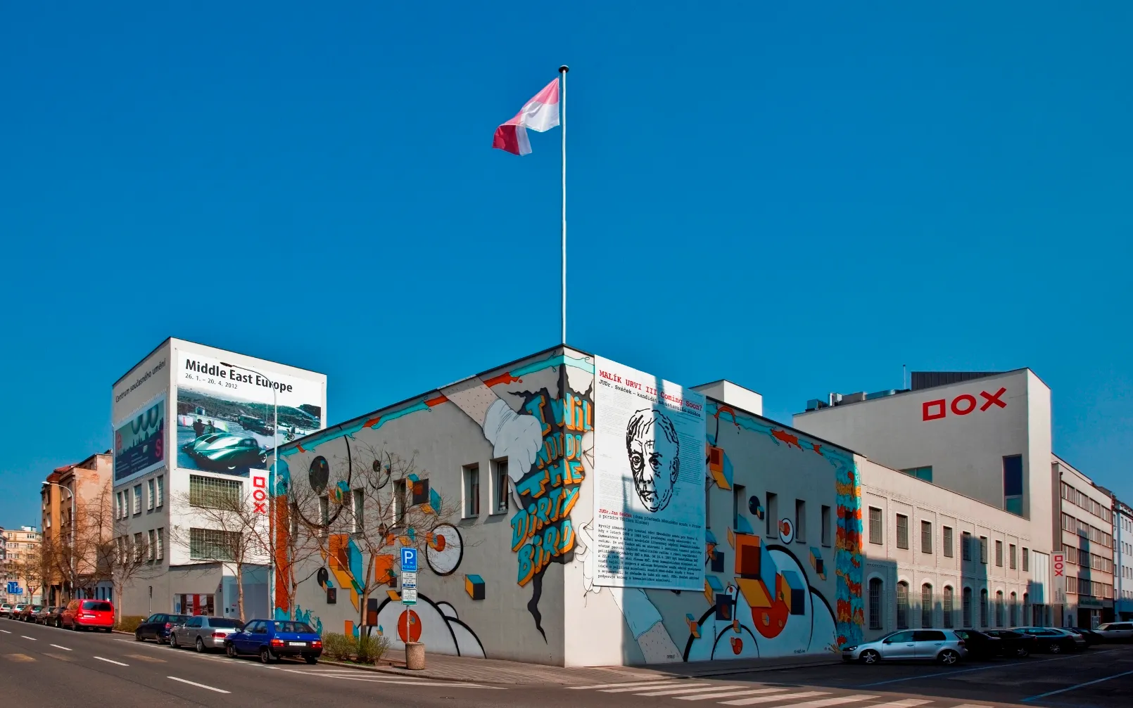 Budynek DOX Centre for Contemporary Art z kolorowym muralem i czeską flagą na maszcie.