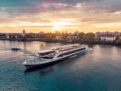 Aerial view of a large river cruise ship on the Rhine river at sunset with Basel cityscape and church tower in the background