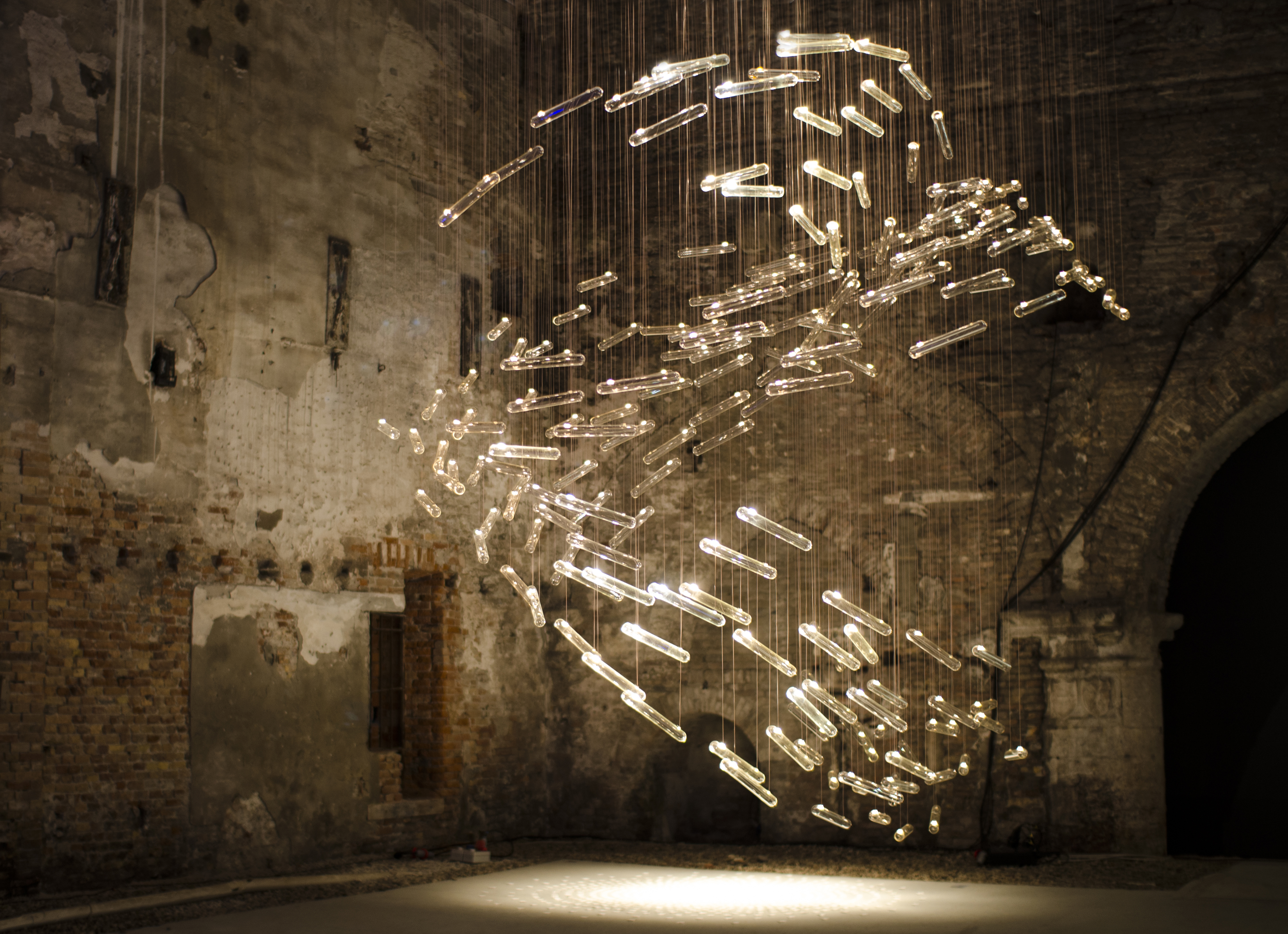 Immersive light installation with suspended illuminated elements in a historic stone building interior with worn walls