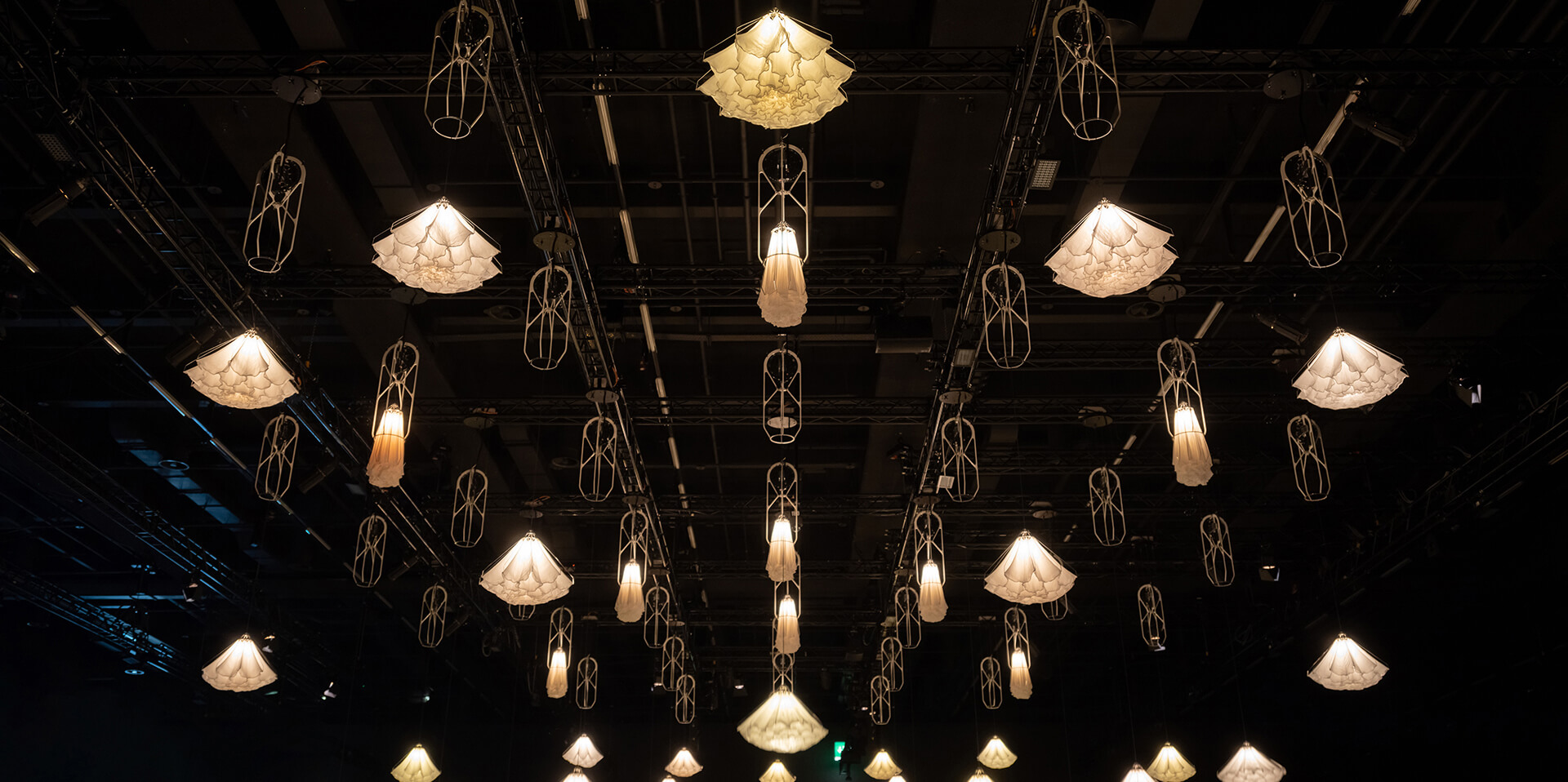 Hanging illuminated geometric light fixtures suspended from a dark ceiling in a dimly lit space