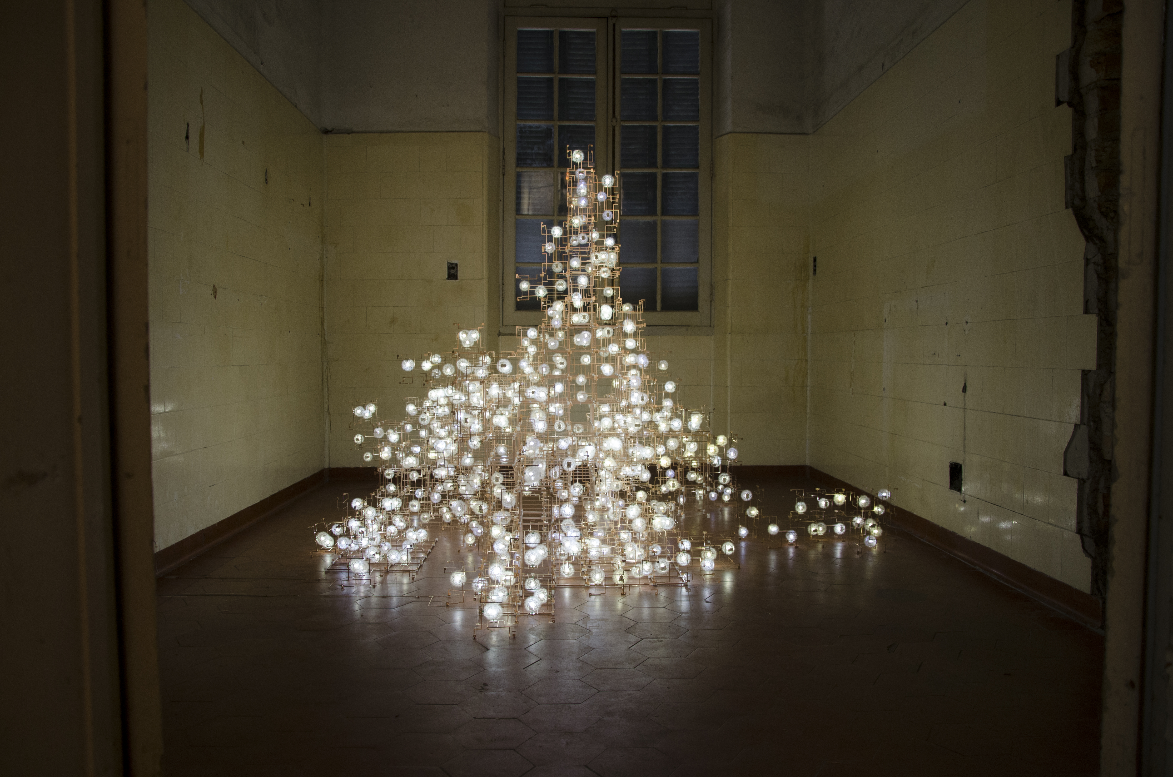 Immersive light installation with hundreds of glowing orbs arranged in a pyramid shape inside a museum gallery room with high ceilings and wooden floors.