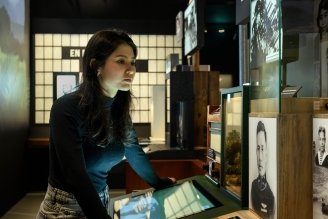 Vrouw die interageert met een digitaal tentoonstellingsscherm, omringd door historische foto's in een schemerige museumgalerij