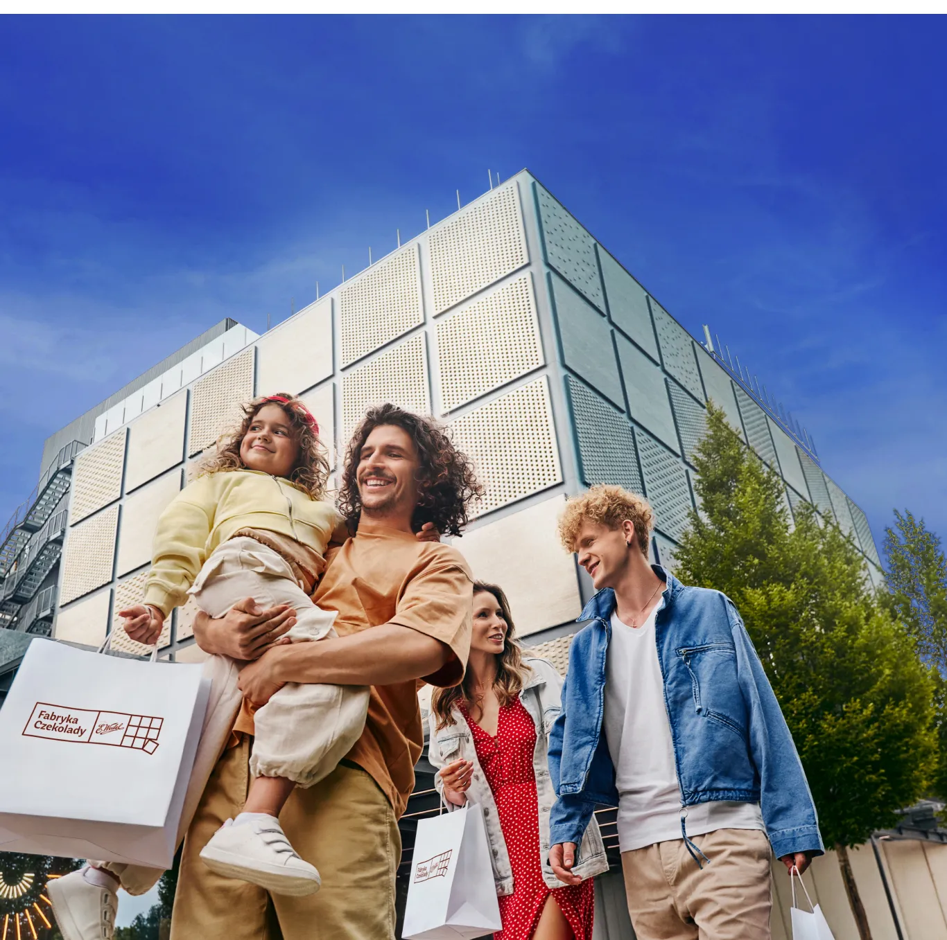 A family of four walking outside a modern building with a geometric facade under a blue sky