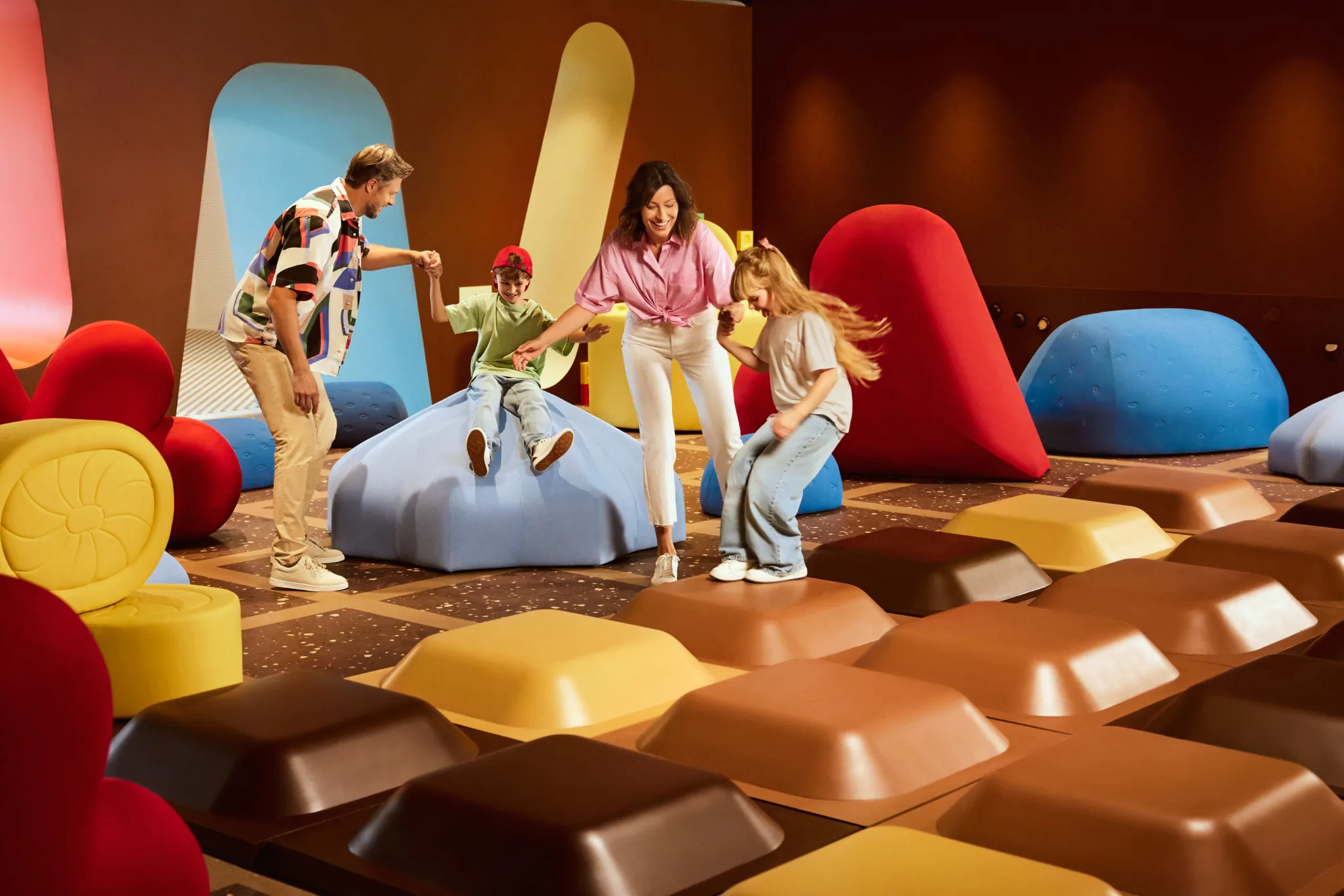 A family playing on large chocolate bar-shaped seats in a colorful indoor exhibit