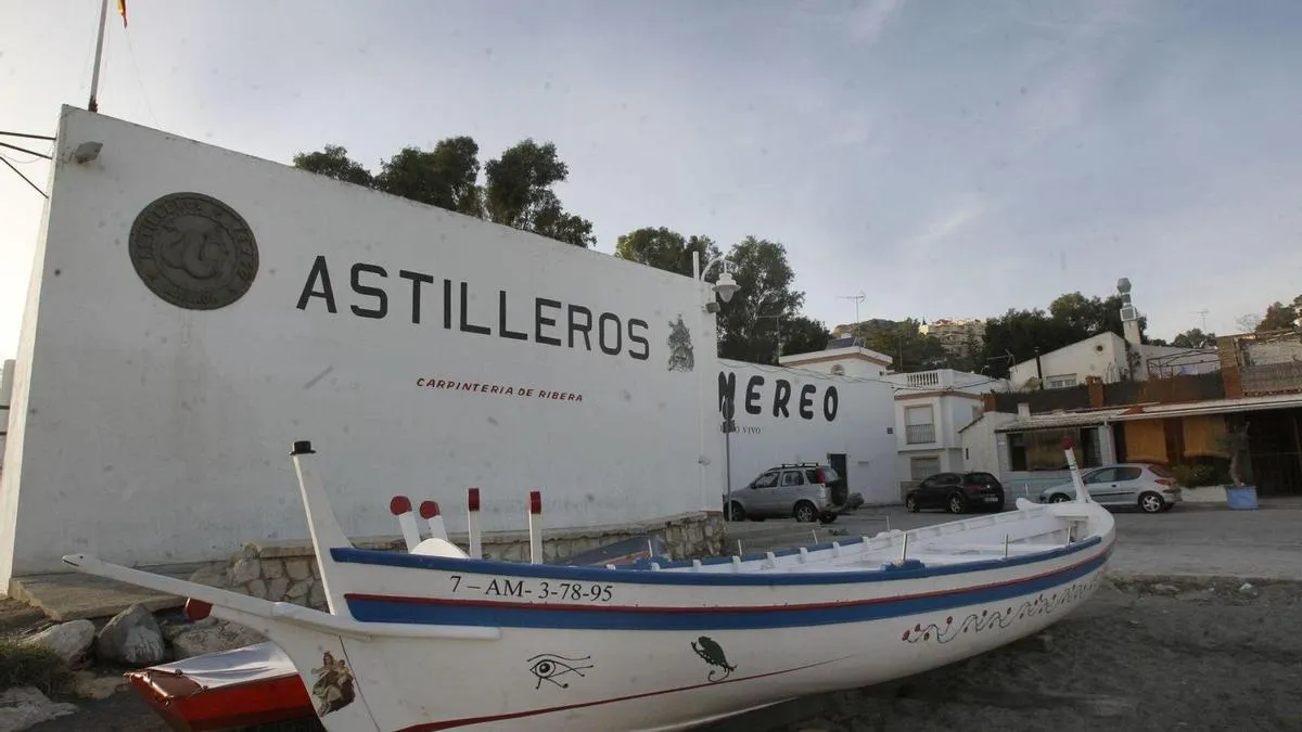 Fachada blanca de un edificio con el texto 'ASTILLEROS NEREO' y un barco pesquero de madera tradicional en primer plano