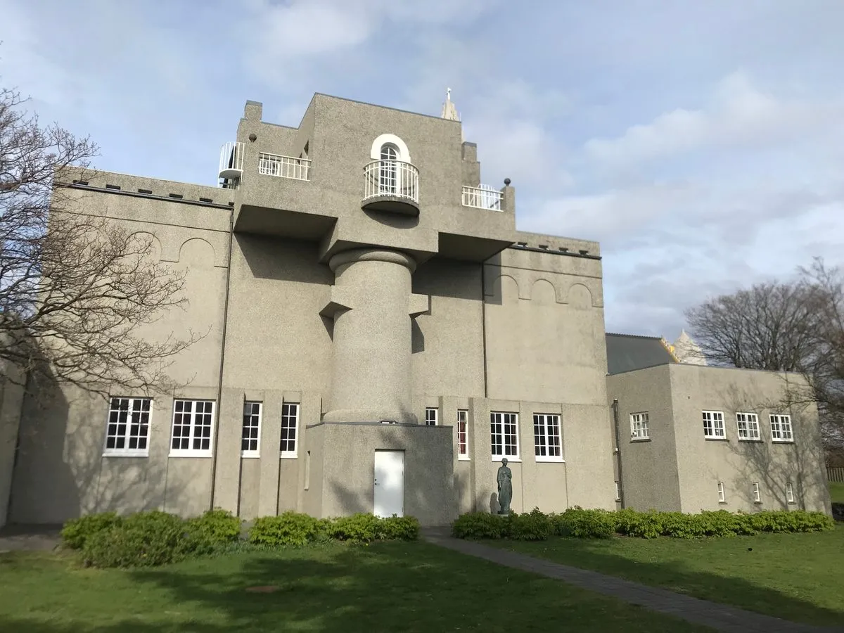 Zewnątrz Einar Jónsson Museum, betonowy budynek z centralnie umieszczoną cylindryczną wieżą z balkonem, białymi drzwiami i otaczającym go trawnikiem.
