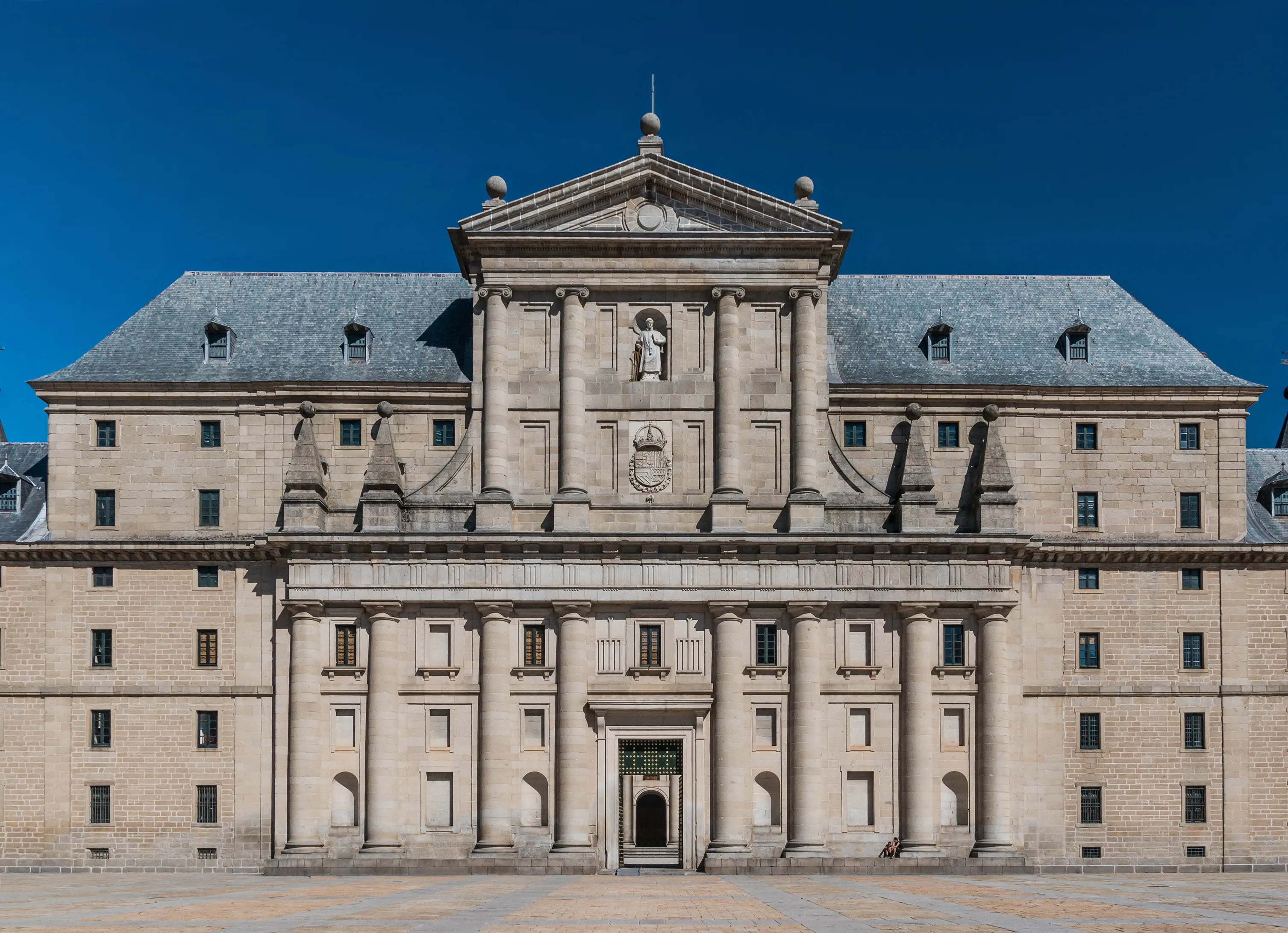 Fasada Królewskiego Kompleksu w San Lorenzo de El Escorial z centralnym wejściem flankowanym kolumnami i symetrycznym projektem pod błękitnym niebem