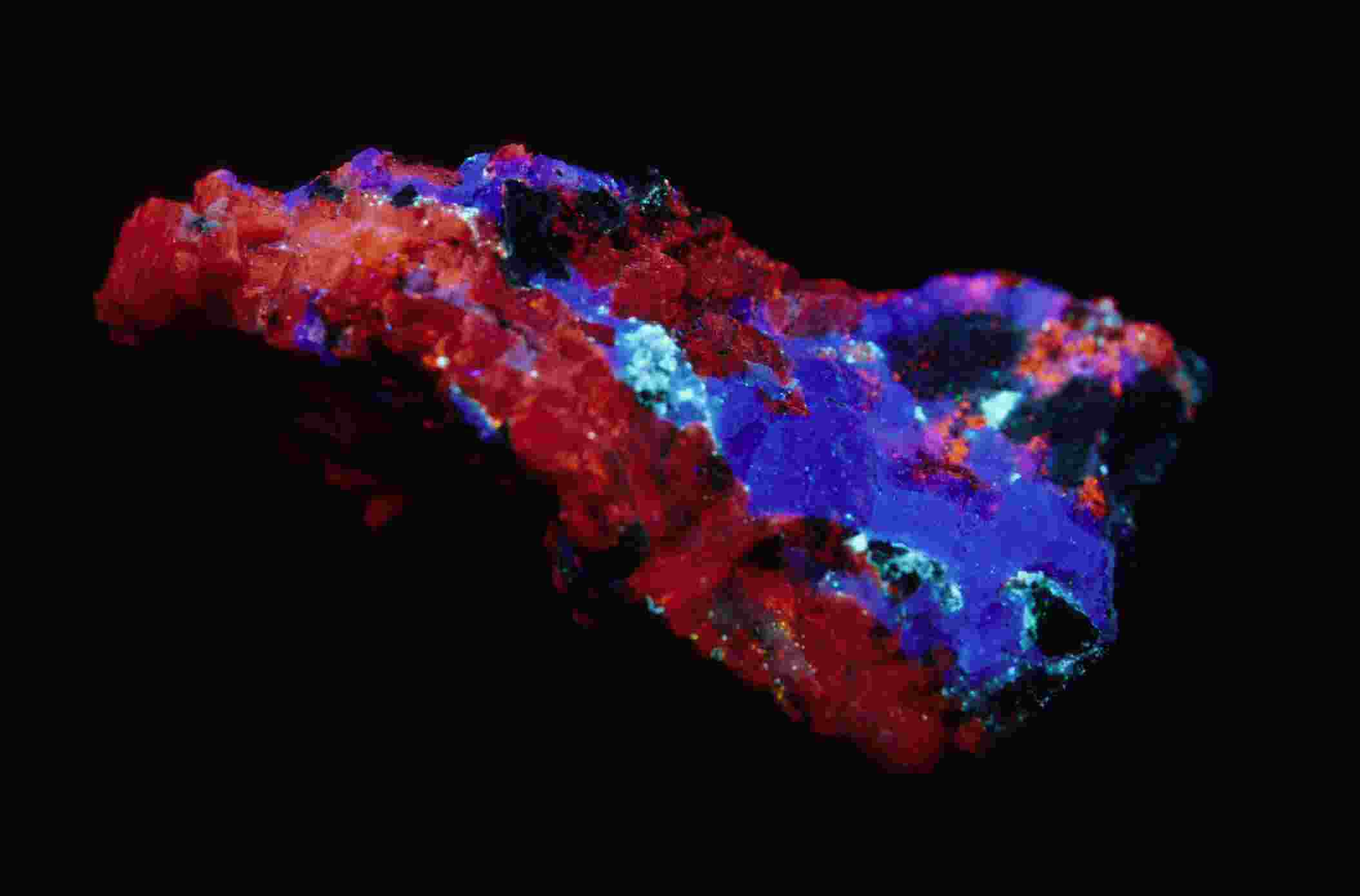 Especimen mineral fluorescente de vibrante color rojo y azul brillando sobre fondo negro