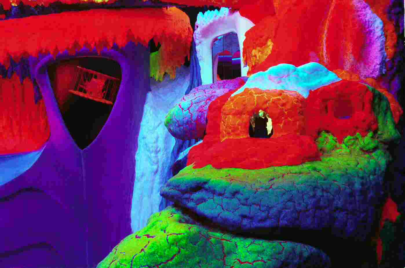 Vibrant fluorescent art installation with textured, glowing surfaces in red, purple, green, and blue under UV lighting