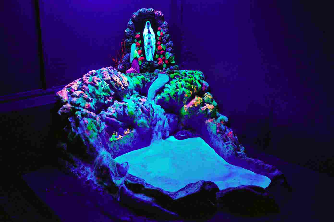 Fluorescent art installation with glowing colorful rock formations and a luminous figure at the top under ultraviolet light.