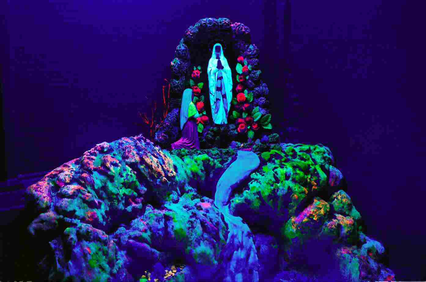 Formación rocosa fluorescente vibrante con figura azul brillante y arreglo floral colorido bajo luz UV