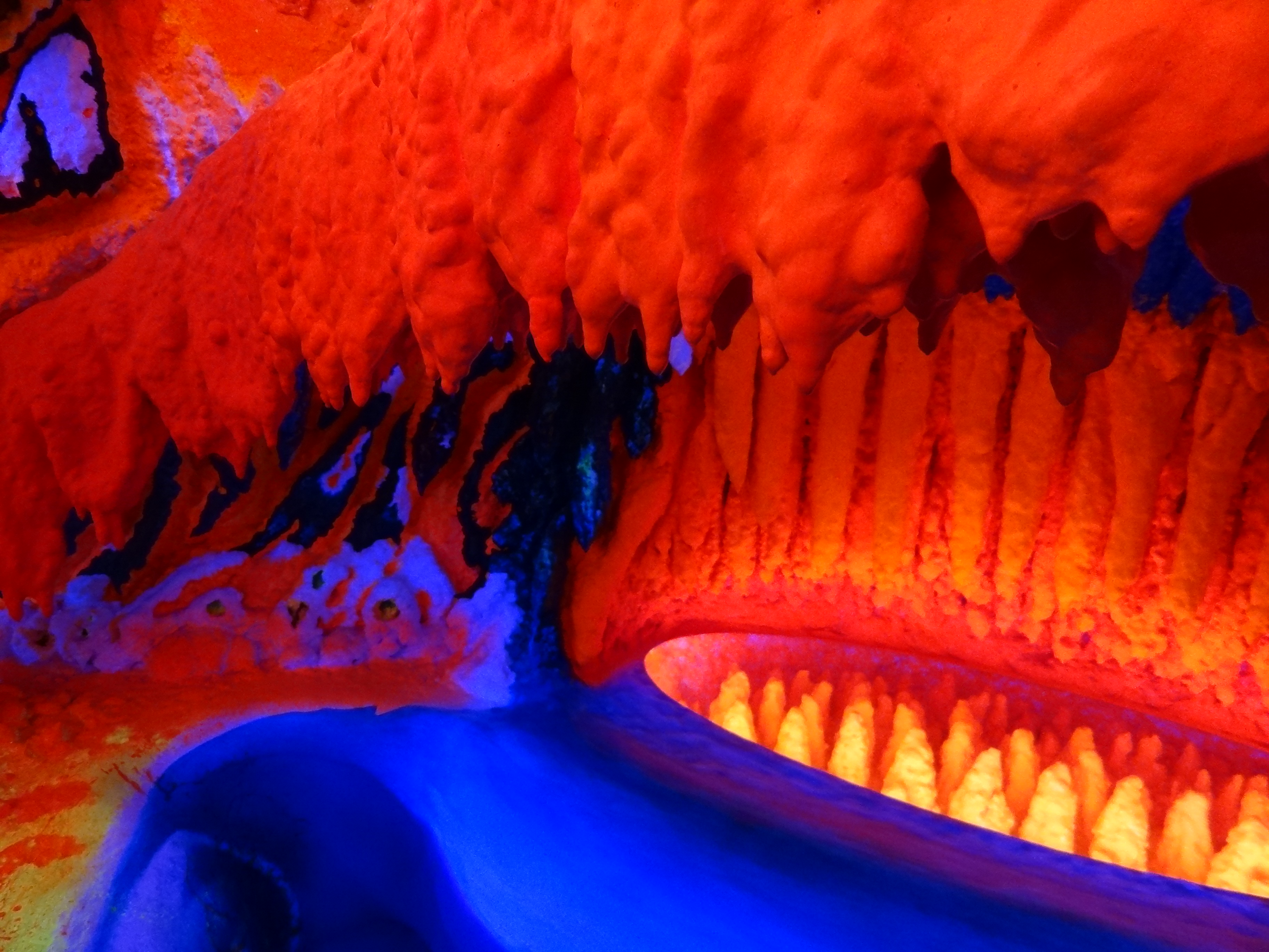 Vibrantes formaciones rocosas de color naranja y azul fluorescente en una instalación de arte inmersiva con estructuras brillantes similares a estalactitas