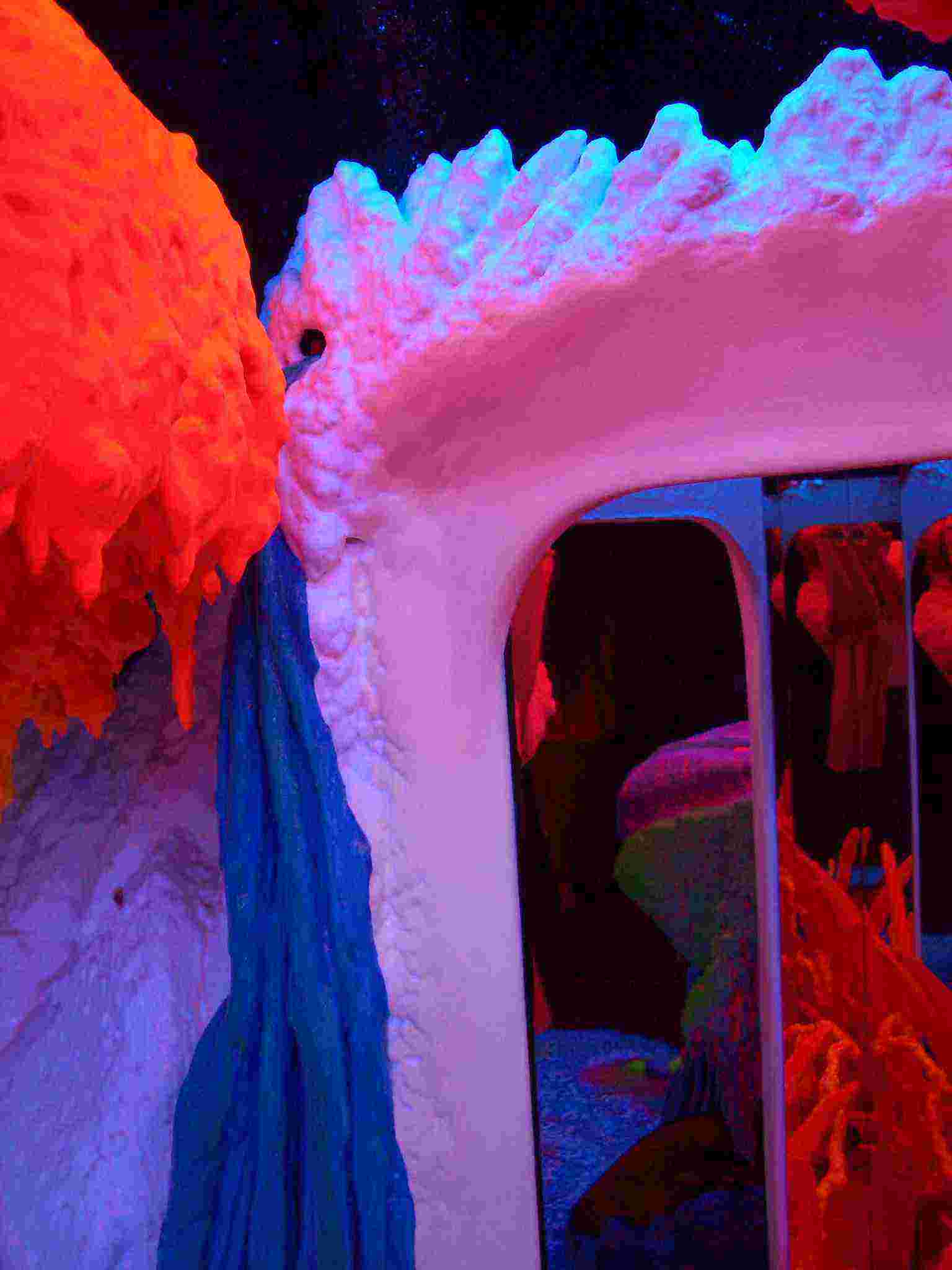 Vibrante instalación de arte fluorescente con estructuras texturizadas de color rosa, rojo y azul brillante que forman una puerta arqueada en un entorno oscuro