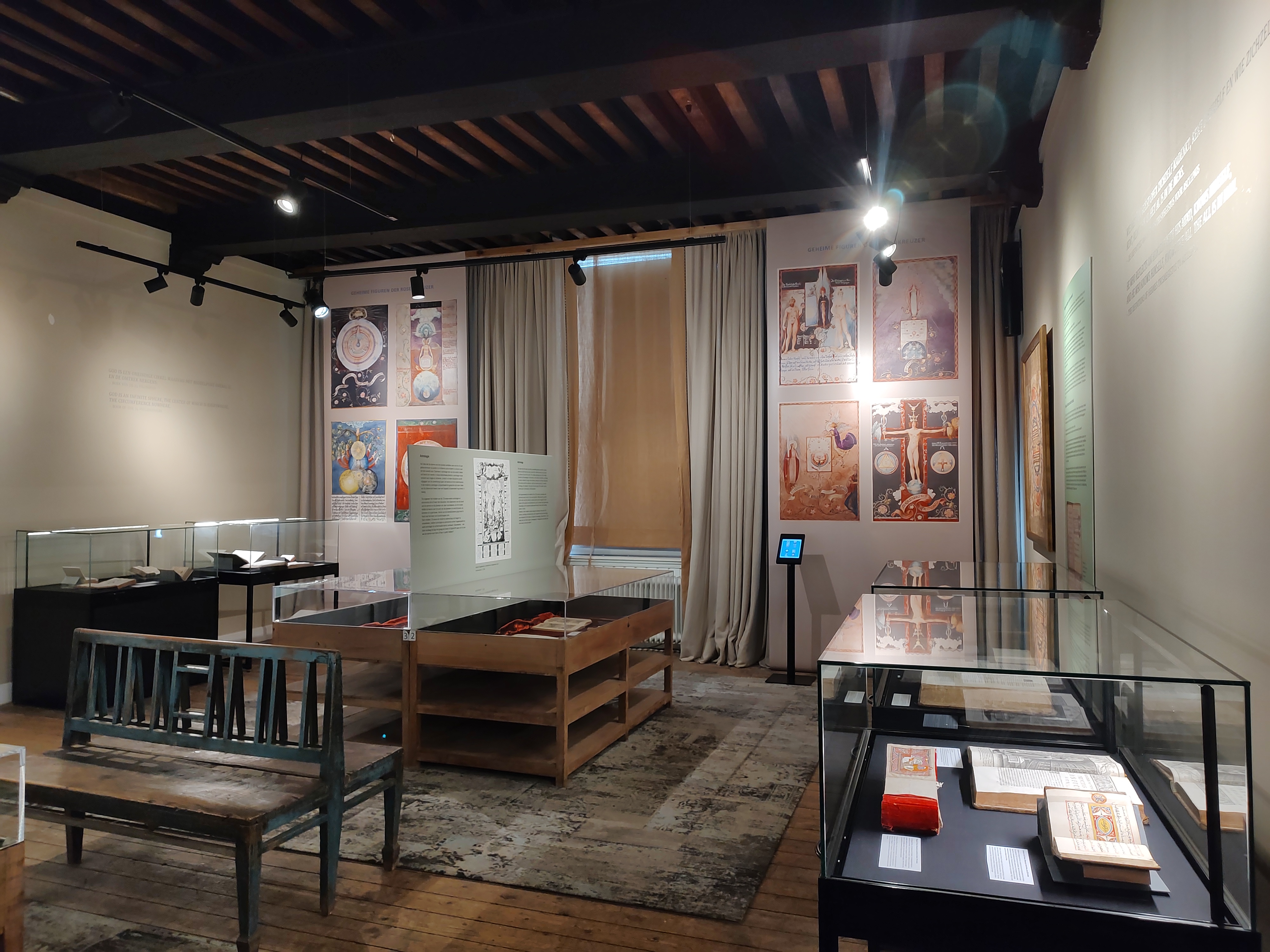 Interior de museo con vitrinas que contienen libros y manuscritos, mesas de madera, bancos y carteles históricos en las paredes