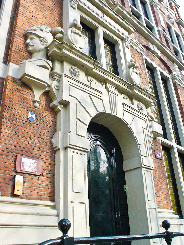 Fachada ornamentada de ladrillo con puerta arqueada, tallas de piedra y escultura de busto sobre la entrada del edificio histórico de Ámsterdam Huis met de Hoofden.