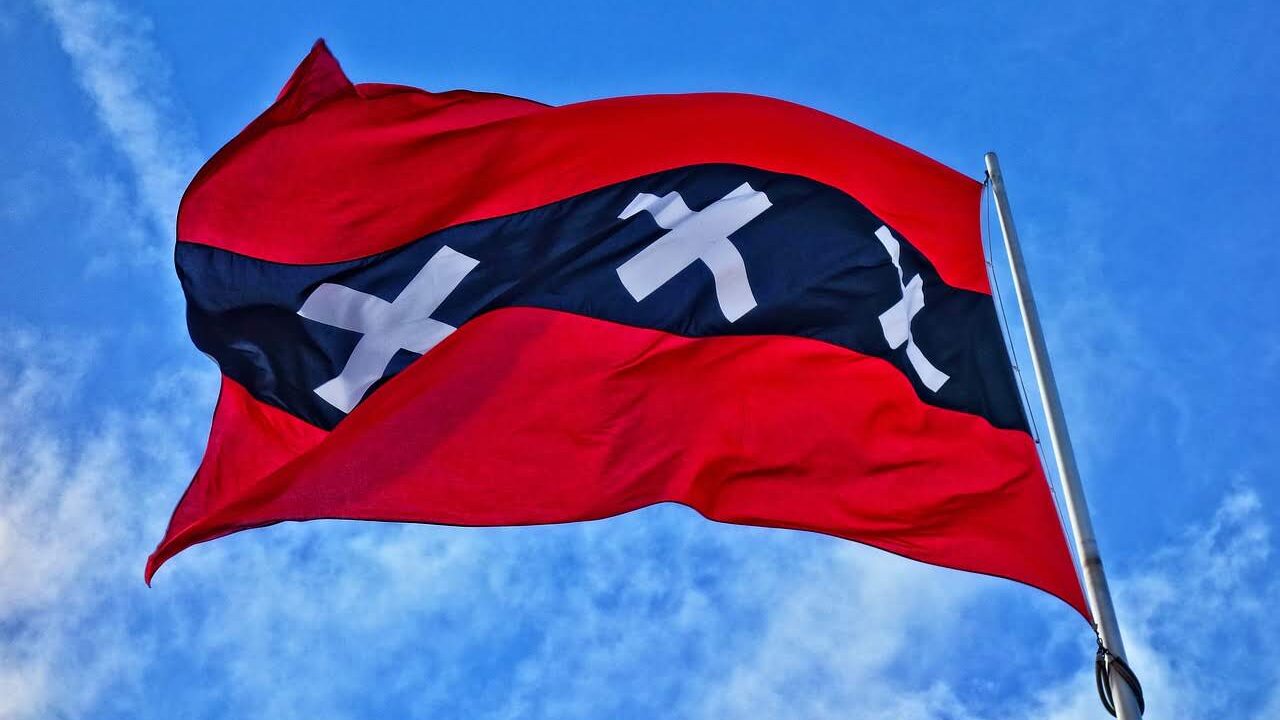 Bandera a rayas rojas y negras con cruces blancas ondeando contra un cielo azul