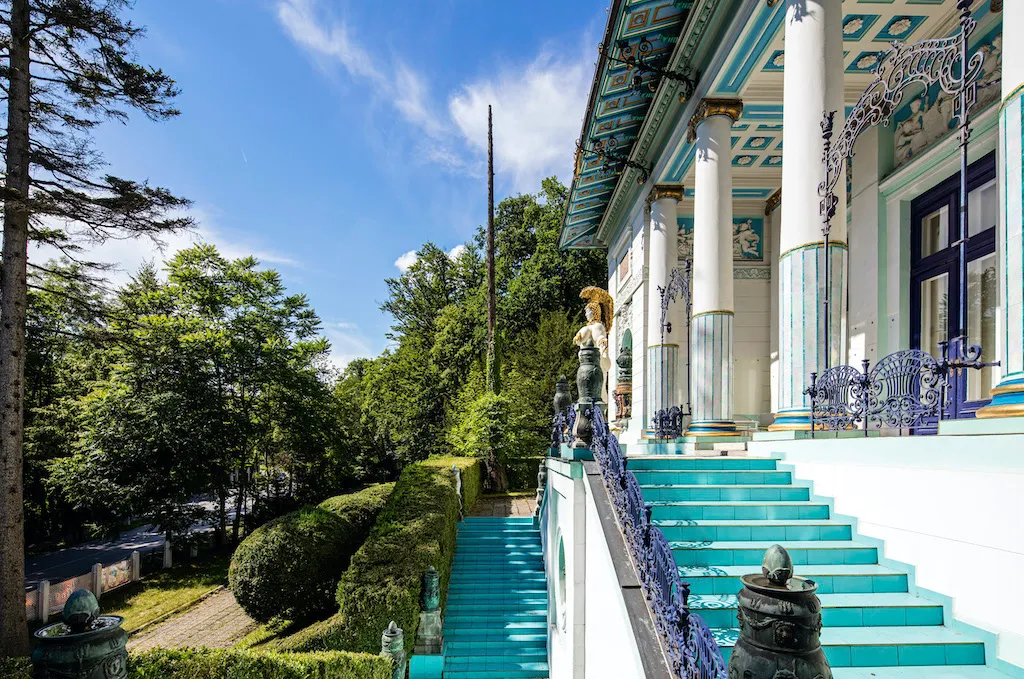 Villa Wagner I con escalones turquesa y ornamentadas columnas blancas bajo un cielo azul