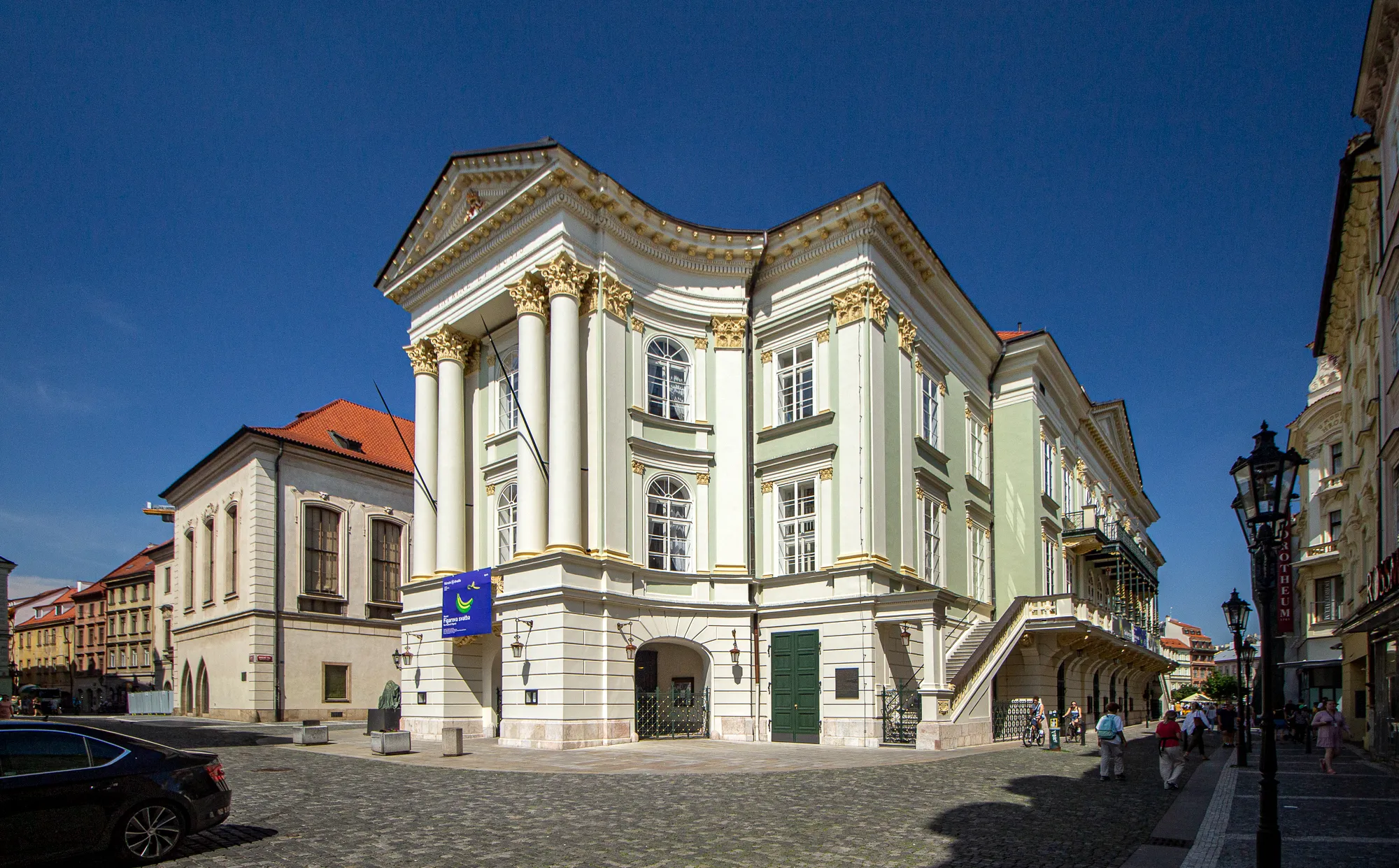 The Estates Theatre, a historic building with white and pale green facades, classical columns, and a blue sky overhead