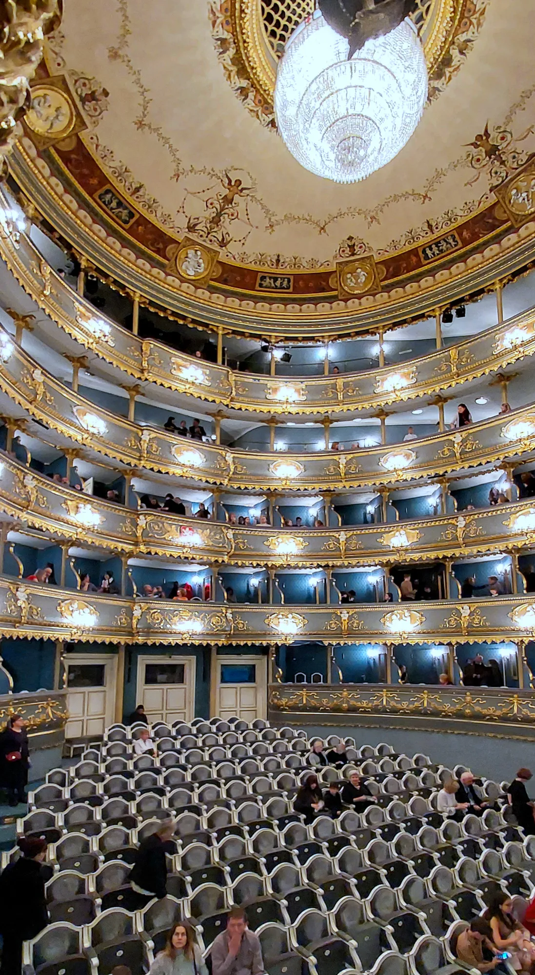 Interior of the Estates Theatre with ornate balconies, a chandelier, and audience members