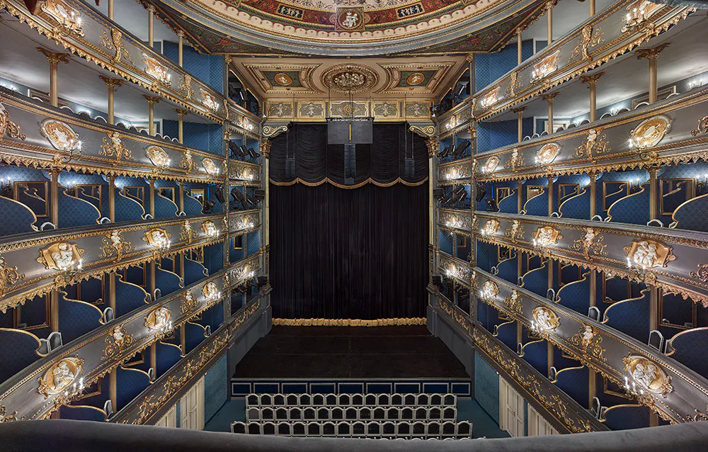 Interior of the Estates Theatre with blue seats, gold accents, and multiple levels of balconies.