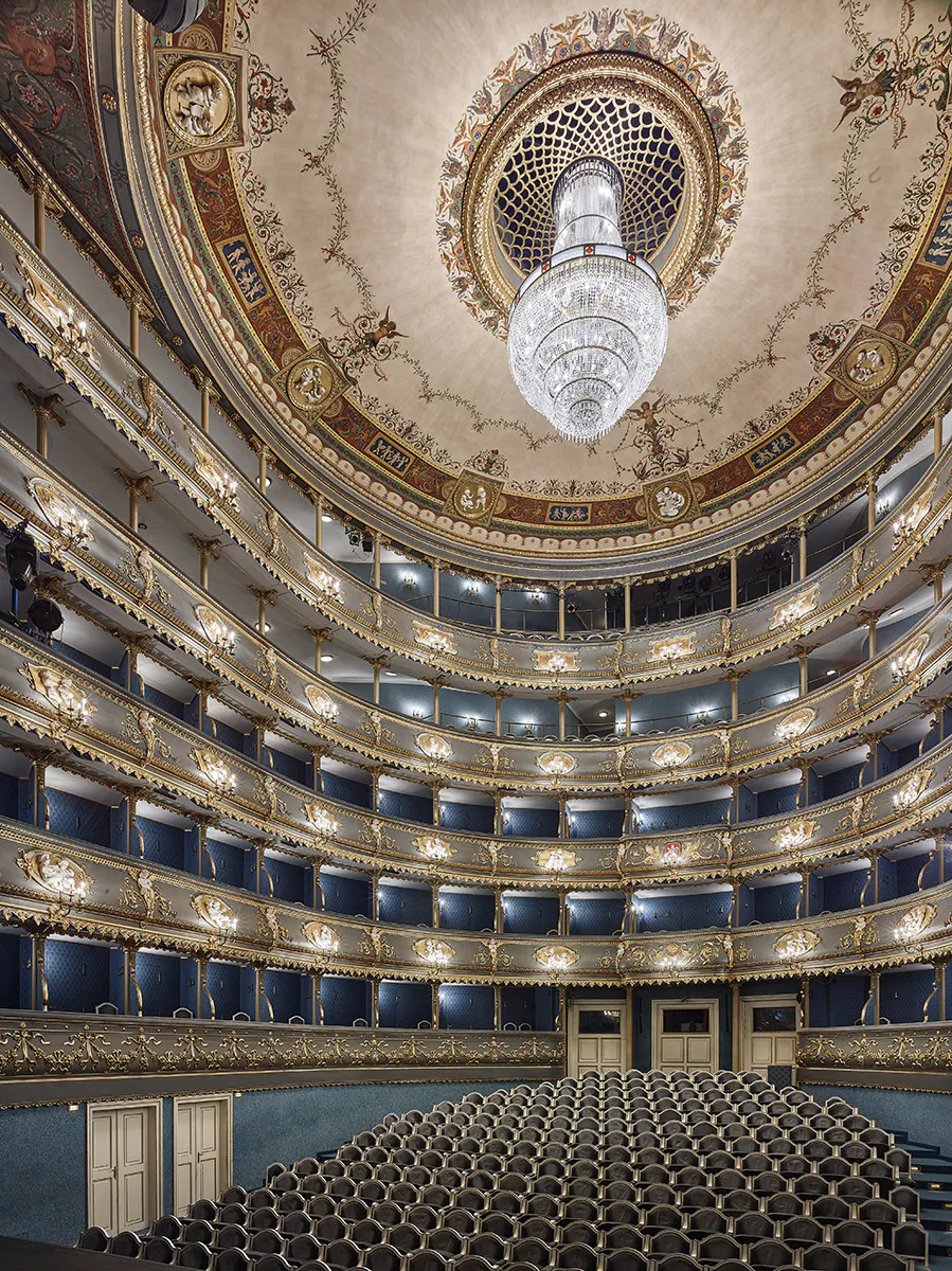 Interior of the Estates Theatre with ornate balconies, a large chandelier, and a decorated ceiling