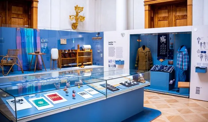 Vitriñas de cristal con artesanía y artefactos folclóricos checos tradicionales, paredes azules y maniquíes en una galería de museo.