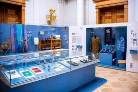 Interior del Museo de Etnografía con vitrinas de cristal, paredes azules y ropa tradicional en maniquíes.