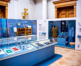 Tentoonstellingsdisplay met vitrines met traditionele Tsjechische volkskledij en ambachten, blauwe muren en informatieve panelen in een museumgalerij.