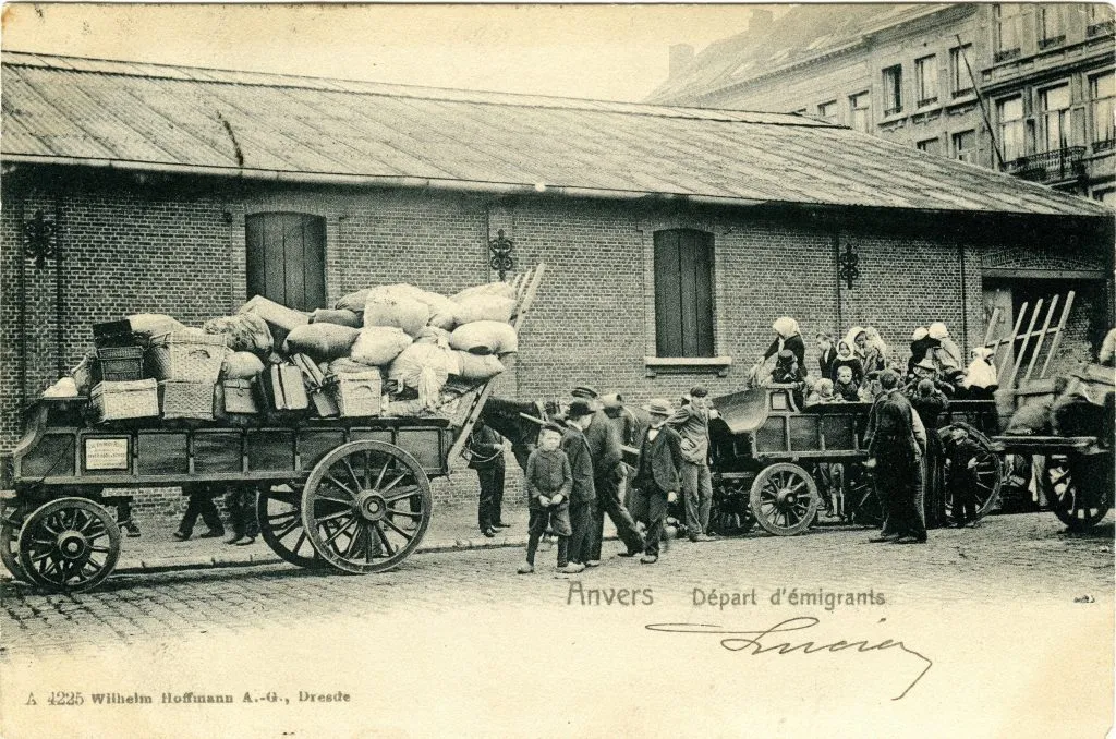 Postal vintage en sepia que muestra a emigrantes con carretas cargadas de equipaje partiendo de un edificio de ladrillo en Amberes, etiquetada como 'Anvers Départ d'émigrants'