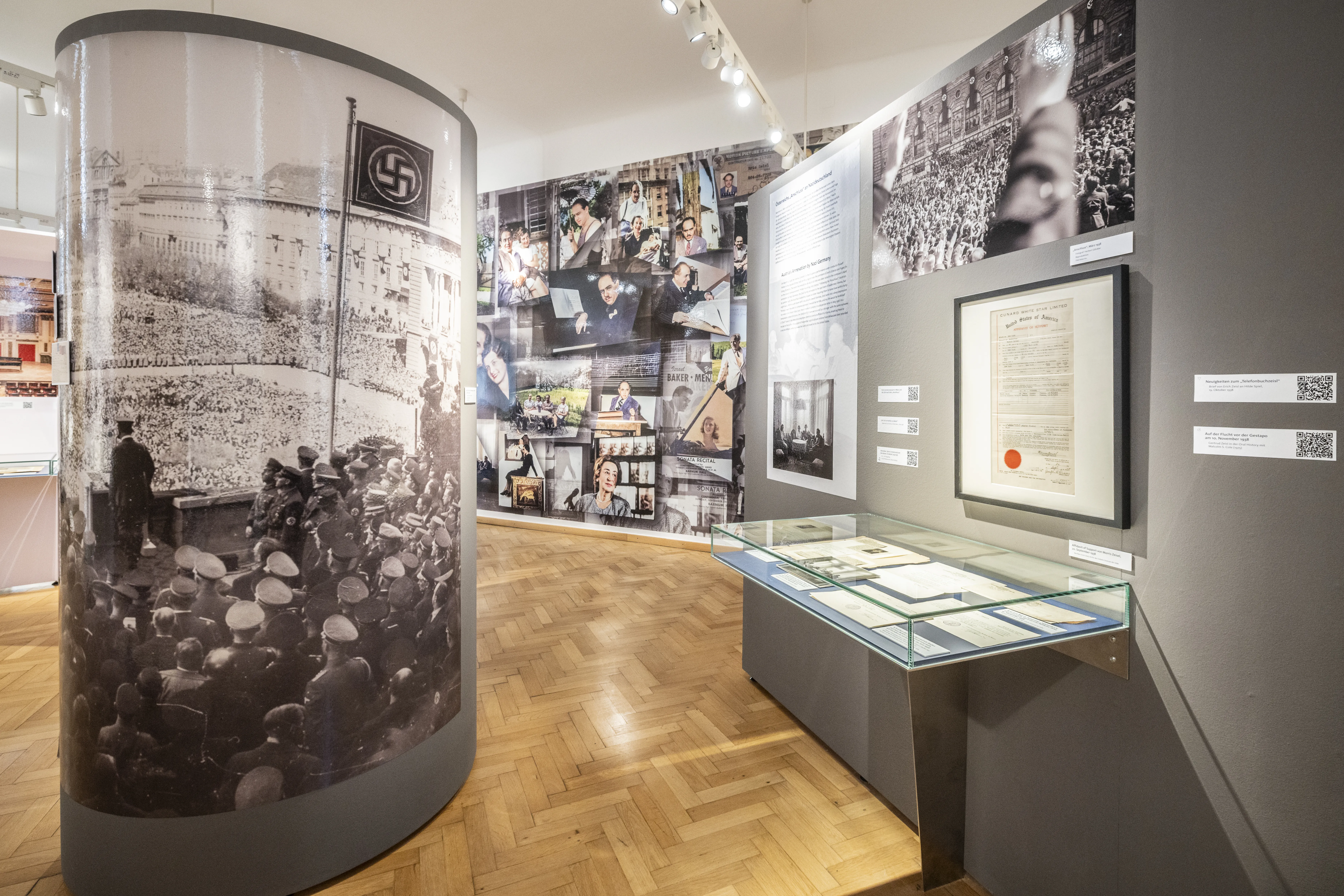 Wnętrze wystawy muzealnej z cylindryczną gablotą, szklanymi gablotami i historycznymi fotografiami na ścianach