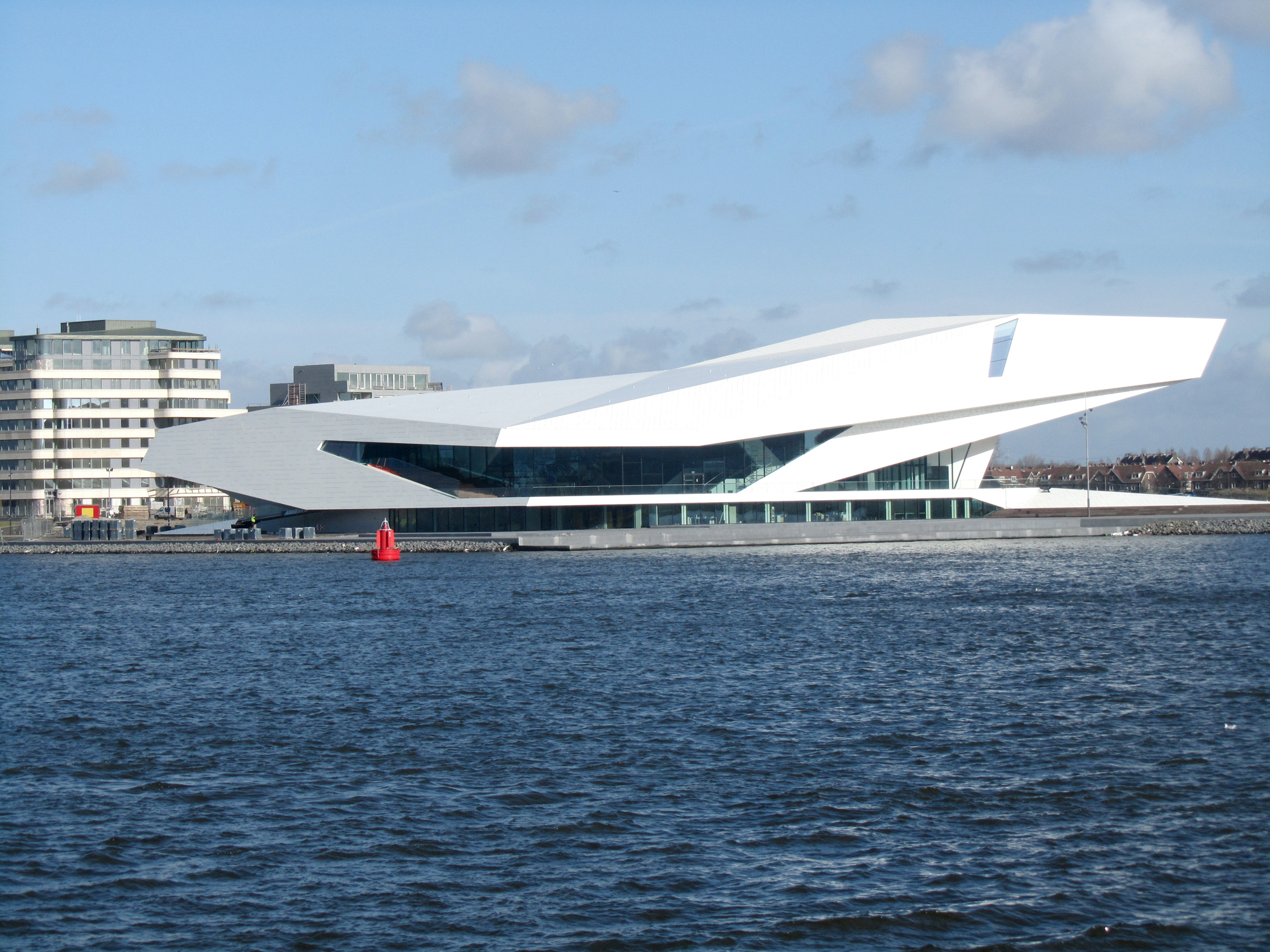 Modern white angular building of Eye Filmmuseum along waterfront with blue sky and water in foreground