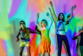 Children dancing with arms raised against a vibrant, multicolored gradient backdrop