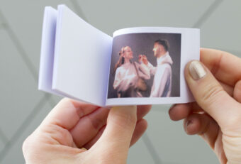 Hands holding a small photo album open to an image of two people in a vintage film scene